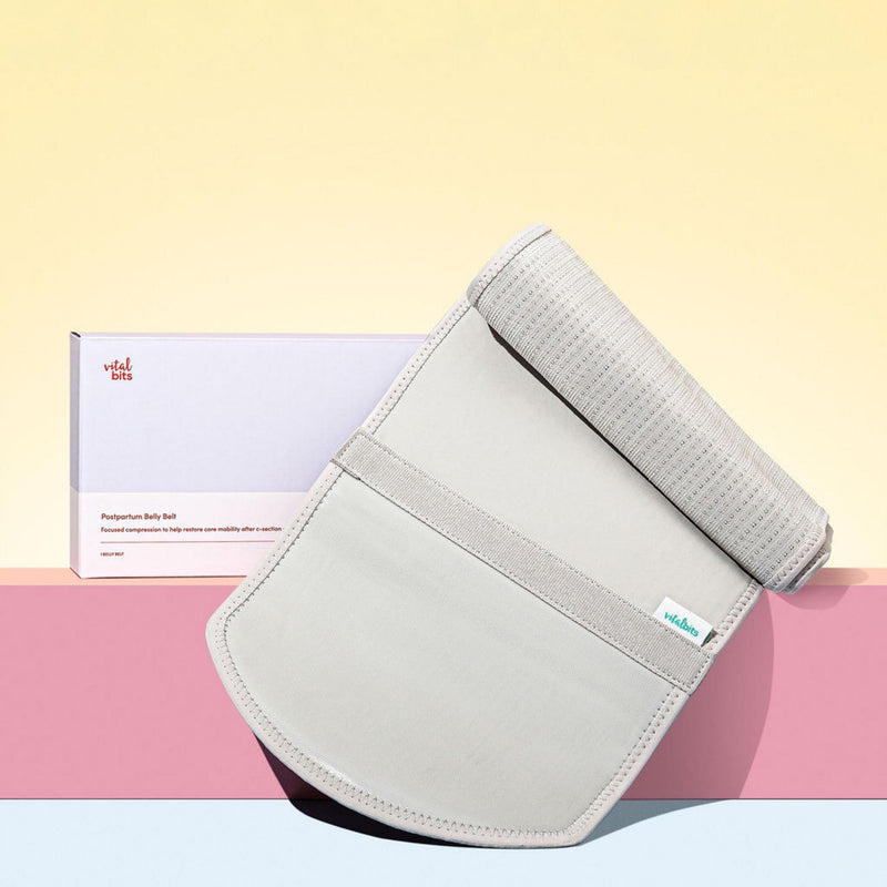 Grey abdominal support binder with a box labeled 'Vital Bits' on a pink and yellow gradient background