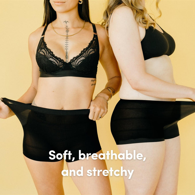 Two women wearing black disposable postpartum briefs who are pulling at their waistbands with a yellow background and text 'Soft, breathable, and stretchy'.