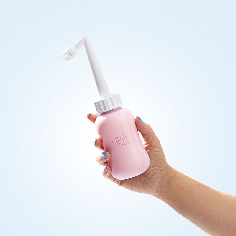Hand holding a purple peri bottle with a white nozzle on a light blue background
